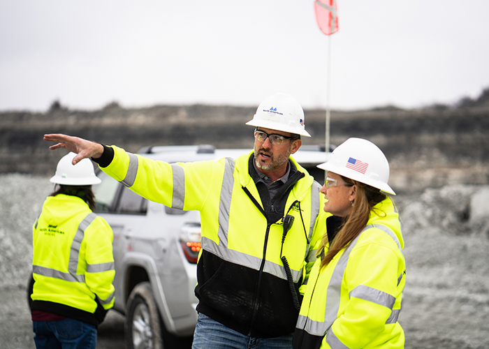 Two North American Mining employees in safety apparel, hard hats and safety glasses discuss a mine plan looking over the mine.